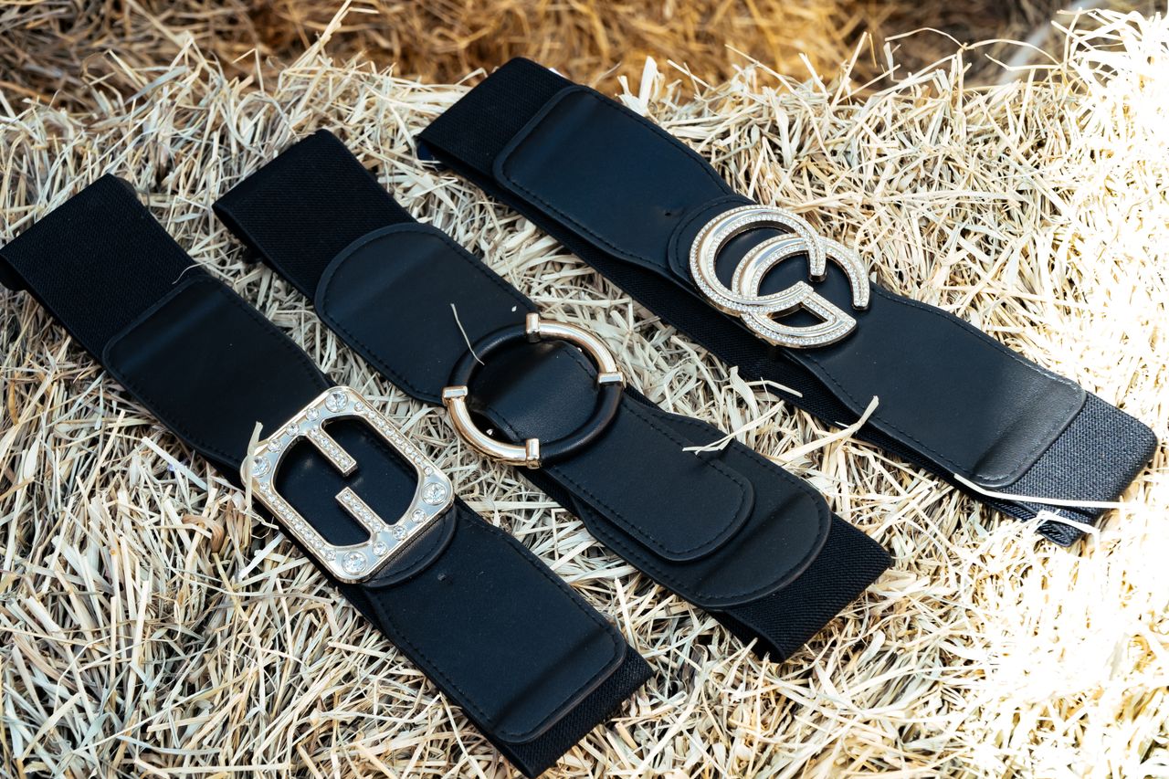 Three black leather belts with decorative metallic buckles displayed on straw background.
