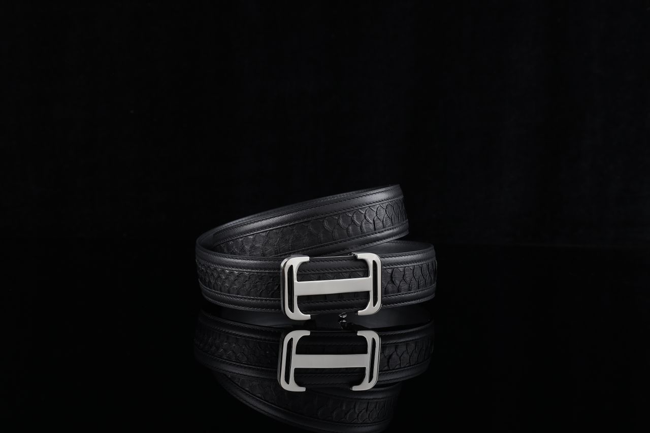 Elegant black leather belt with a silver buckle on a reflective surface, perfect for fashion.