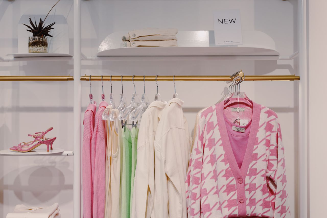 Stylish women's clothing on rack featuring pink cardigan and green dress inside a boutique.